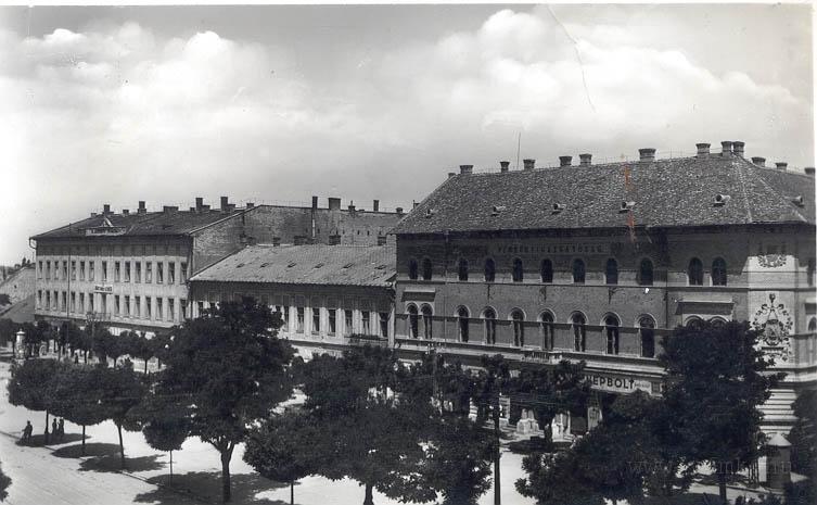 epulet04.jpg - Az L alakú épület levágott sarki falsíkján fent  a magyar címer, középen pedig a pelikános városcímer stukkója látható